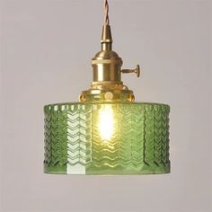 a green glass pendant light hanging from a ceiling fixture with a gold finish on the top