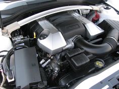 the engine compartment of a white car with its hood open and it's lights on