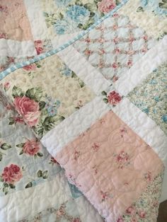 an old quilt is laying on top of a bed with pink and blue flowers in it