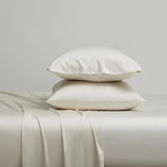 two white pillows sitting next to each other on top of a bed covered in sheets