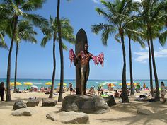 a statue of a man holding a surfboard in front of palm trees on the beach