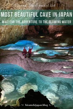 two people standing in the middle of a cave with blue water and green moss growing on it