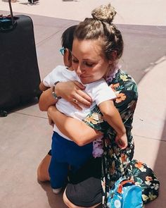 a woman sitting on the ground holding a small child in her arms with luggage behind her