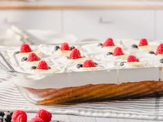 a cake with berries and cream on top in a glass dish next to raspberries