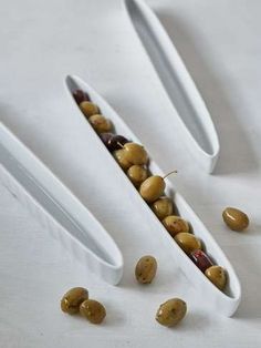 three white bowls filled with olives and other food items on a white tablecloth