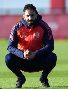 a man kneeling down on top of a soccer field with his hands in his pockets