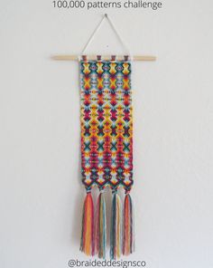 a wall hanging with multicolored beads and tassels hangs on a white wall