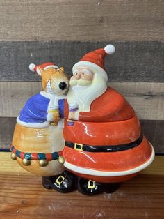 santa and mrs claus sitting on top of a wooden table next to eachother