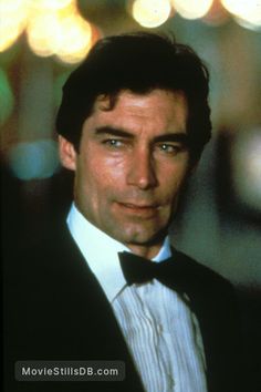 a man in a tuxedo and bow tie looking at the camera with blurry lights behind him