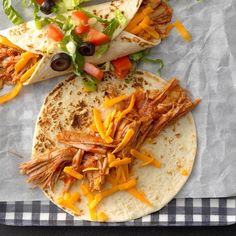 three tacos with shredded meat, cheese and lettuce on them sitting on a checkered table cloth