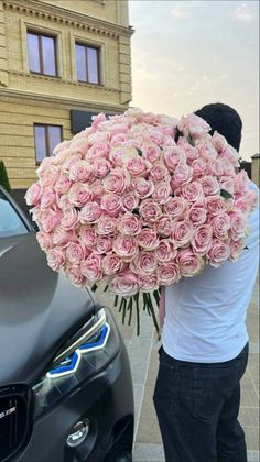 a man holding a large bouquet of pink roses in front of a black bmw car