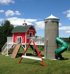 a red barn with a slide and play set in the grass next to a tall gray silo