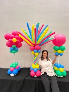 a woman sitting in front of balloons on a table with black cloth and white backdrop