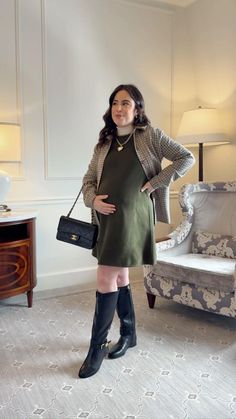 a woman standing in front of a chair and holding a handbag while wearing knee high boots