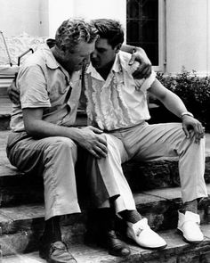 two men are sitting on the steps and one is holding his hand over another man's shoulder