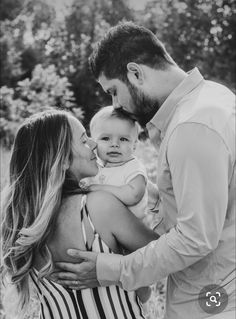 a man holding a baby in his arms while standing next to a woman with her arm around him