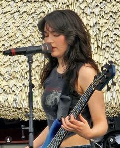 a woman holding a guitar while standing in front of a microphone