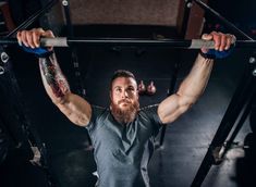 a man with a beard is doing pull ups on a bar in the gym while looking at the camera