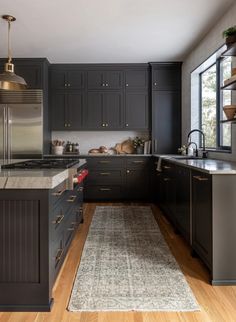 a large kitchen with black cabinets and wooden flooring, along with a rug on the floor