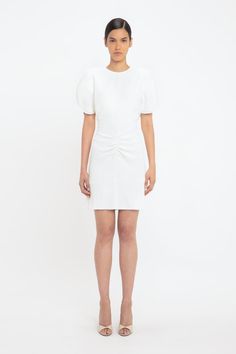 a woman standing in front of a white background wearing a short dress with an asymmetric