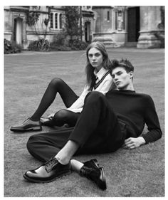 two people sitting on the ground in front of a building and one person wearing black shoes