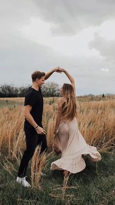 a man and woman dancing in the middle of a field with tall grass behind them