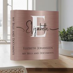 a pink book sitting on top of a wooden table next to a potted plant