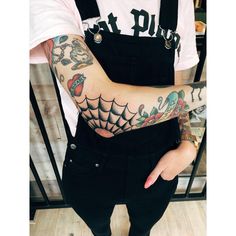 a person with tattoos on their arm and arms holding something in one hand while wearing black overalls