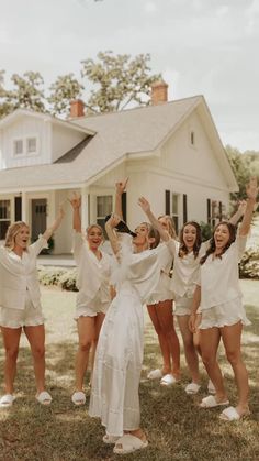 a group of women standing next to each other in front of a white house with their hands up