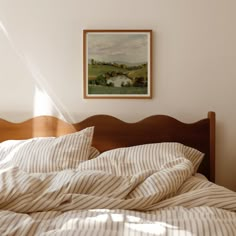 an unmade bed in a bedroom with a painting on the wall