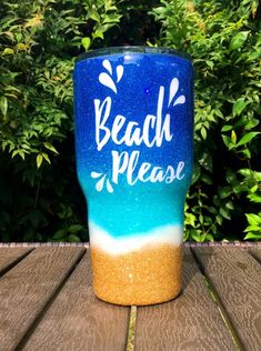 a blue and yellow tumbler with the words beach please on it sitting on a wooden table