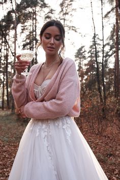 a woman in a white dress holding a wine glass and wearing a pink cardigan