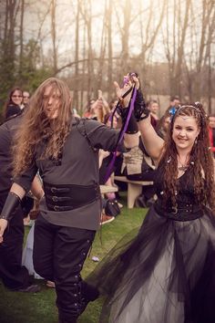 two people dressed up in costume walking through a field with other people behind them holding hands