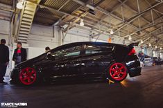 a black car with red rims parked in a garage next to other people standing around