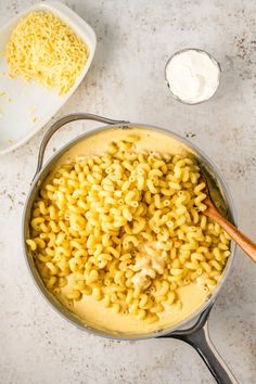 macaroni and cheese being cooked in a pot with a wooden spoon next to it