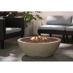 a fire pit sitting on top of a cement floor next to two chairs and a plant