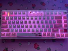 a pink keyboard with hello kitty on the back lit up in purple light, sitting on a flowery surface