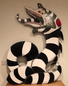 a large black and white snake sculpture on top of a wooden shelf next to a wall