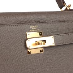 This Kelly, in the Sellier style, is in Etain epsom leather with gold hardware and has tonal stitching, front flap, two straps with center toggle closure, clochette with lock and two keys a single rolled handle and removable shoulder strap.The interior is lined with Etain chevre leather and has one zip pocket with an Hermes engraved pull and two open pockets on the opposite side.Collection: YOrigin: FranceCondition: New and never worn (plastic on hardware)Accompanied by: Hermes box (slightly damaged), Hermes dustbag, clochette, lock, two keys, shoulder strap, clochette dustbag, shoulder strap dustbag, felt and rainhatMeasurements: 11.25" width x 8.25" height x 4.75" depth; 3.5" handle drop (16.5" shoulder strap drop) Formal Epsom Leather Bag With Brass Hardware, Hermes Kelly Sellier, Fendi Jewelry, Kelly Sellier, Prada Jewelry, Hermes Birkin 25, Hermes Birkin 30, Hermes Box, Birkin 25