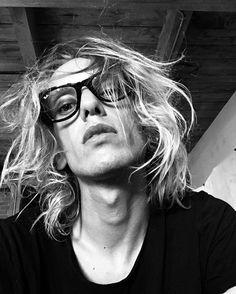 a man with long blonde hair and glasses looking off to the side in black and white