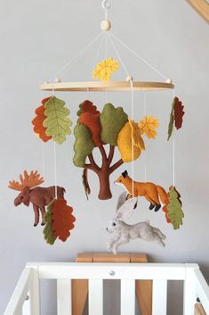 a baby crib with an animal mobile hanging from it's side and trees on the wall