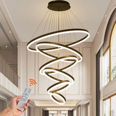 a hand holding a remote control in front of a chandelier with spiral lights