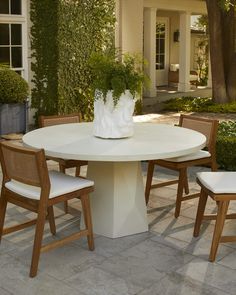 a white table with four chairs around it and a vase sitting on top of the table