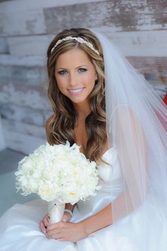 a woman in a wedding dress holding a bouquet of white flowers and posing for the camera