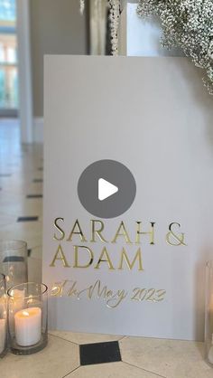 a white sign with gold lettering on it next to candles and vases filled with baby's breath flowers