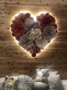 there is a heart made out of flowers on top of a bed with silver pillows