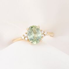 a ring with an oval green stone surrounded by small white diamonds on a white cloth