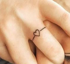 two hands holding each other with tattoos on their fingers and one has a heart in the middle