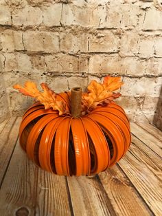 an orange pumpkin sitting on top of a wooden table next to a brick wall with leaves