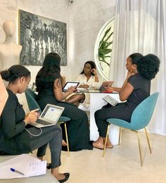 four women sitting at a table with laptops and papers in front of them, talking